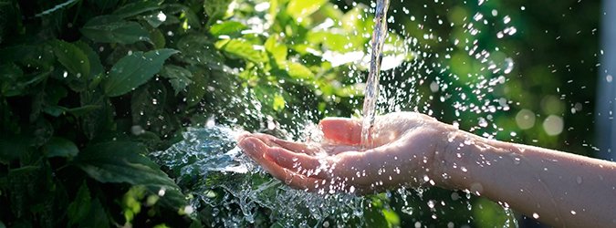 Water pouring in woman hand on nature background, environment issues