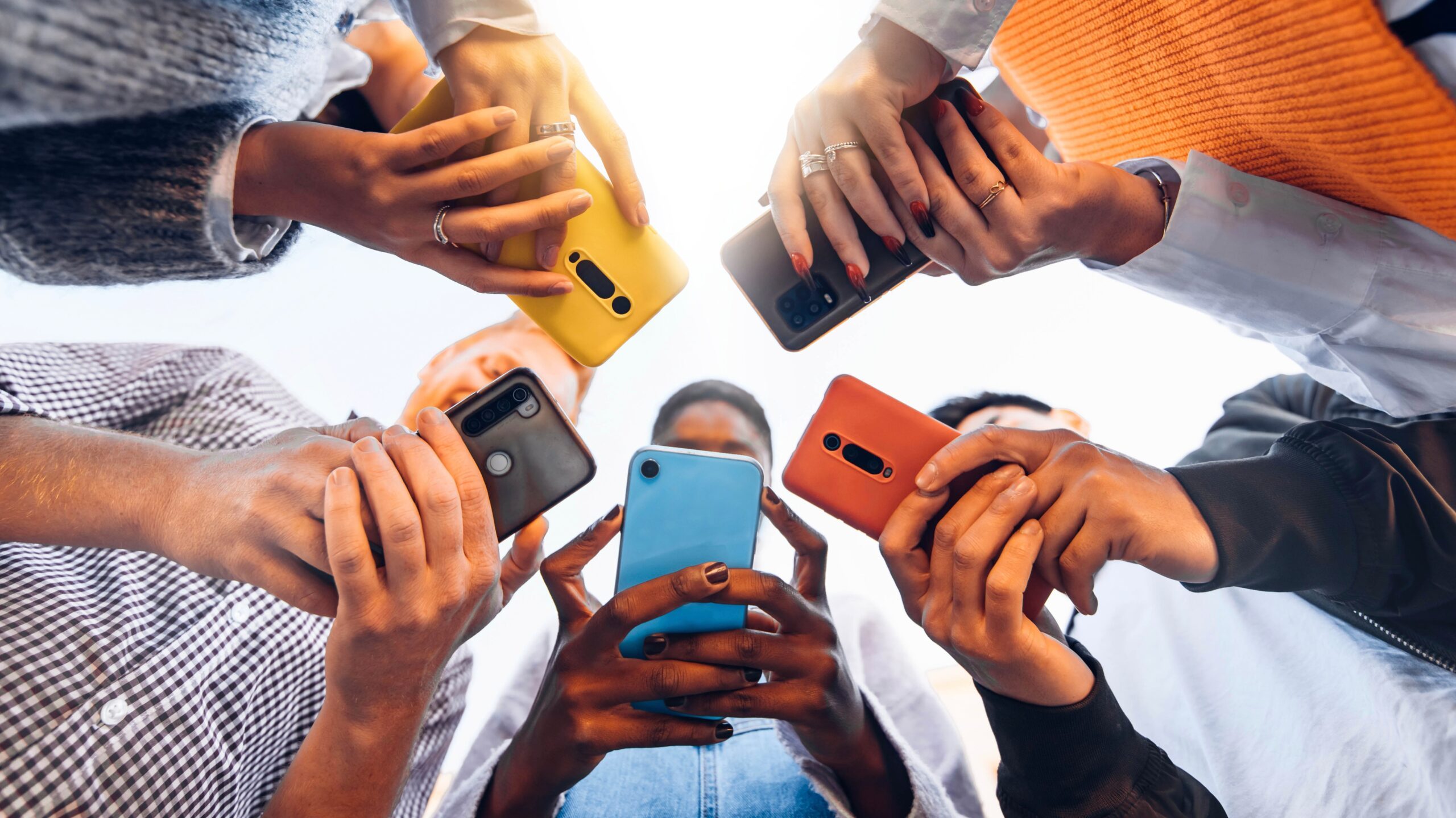 Texting image. Five individuals huddled around their phones while texting.